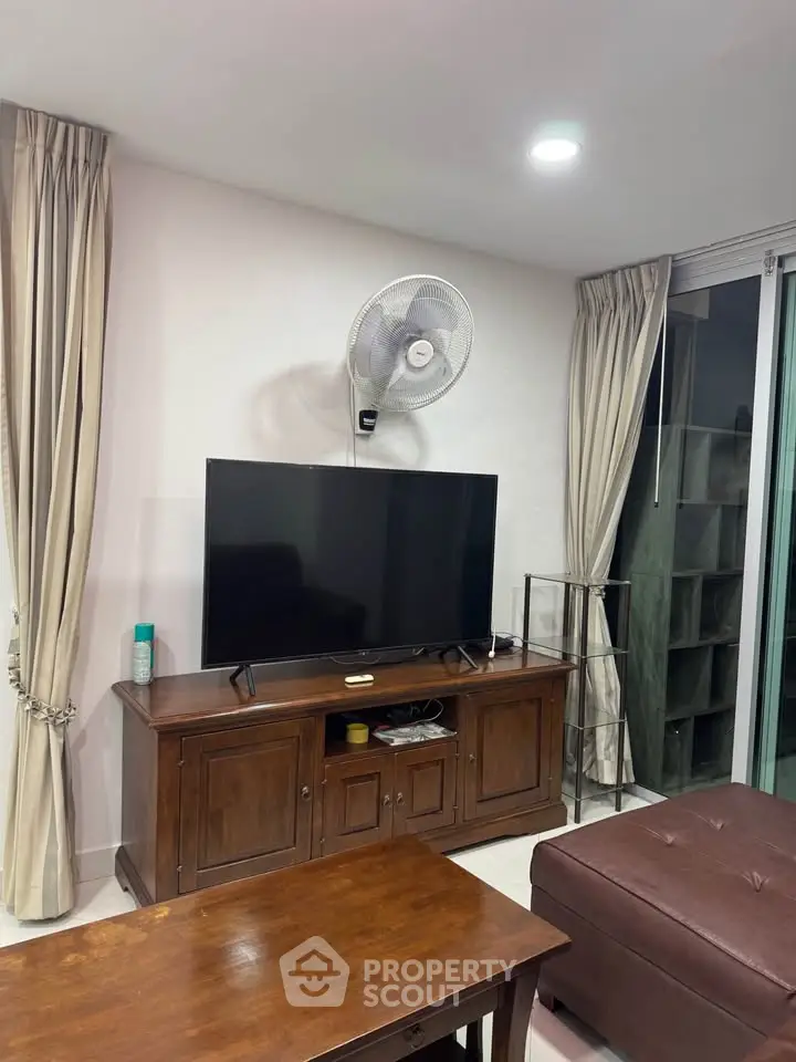 Cozy living room with TV, wooden furniture, and elegant curtains.