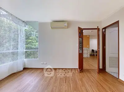Spacious living room with wooden flooring and large window overlooking greenery.
