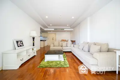 Spacious living room with gleaming hardwood floors, modern furniture, and a seamless transition to an open-layout kitchen.