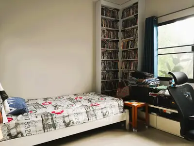 Cozy bedroom with single bed, large window, and extensive bookshelf for a perfect reading nook.