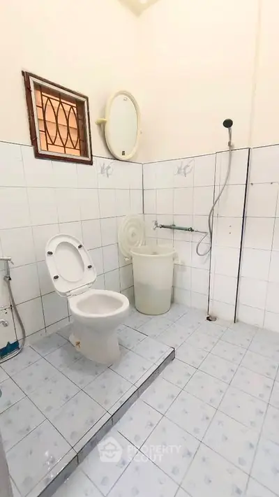 Simple bathroom with white tiles and basic fixtures, featuring a shower and toilet.