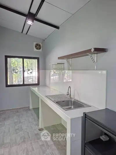 Modern kitchen with sleek design and ample natural light, featuring a stainless steel sink and open shelving.