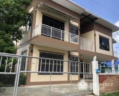 Modern two-story house with balcony and gated entrance in a suburban neighborhood.