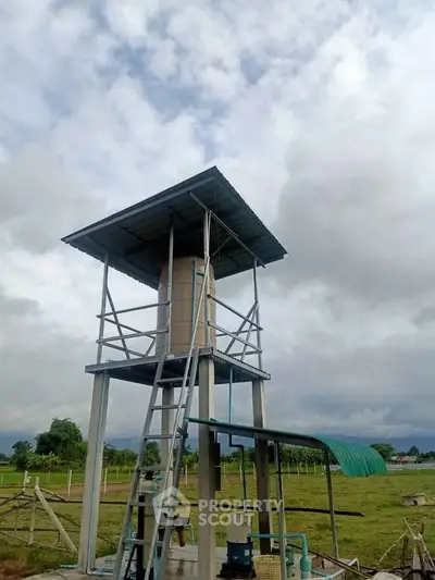 Rural water tower structure in open field with cloudy sky backdrop