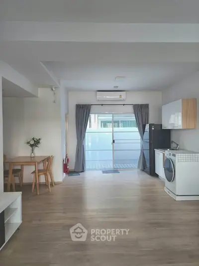 Spacious modern living area with open kitchen and washing machine, featuring wooden flooring and natural light.
