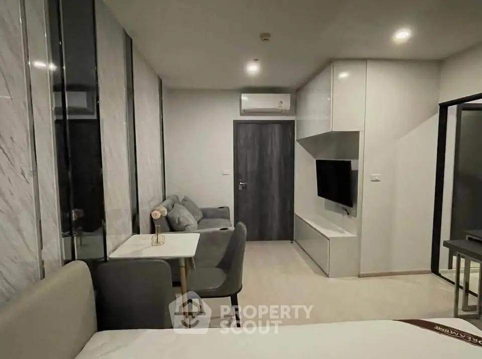 Modern studio apartment with sleek design and cozy furnishings, featuring a wall-mounted TV and stylish dining area.