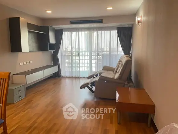 Spacious living room with hardwood floors and reclining chair, featuring large windows with city view.