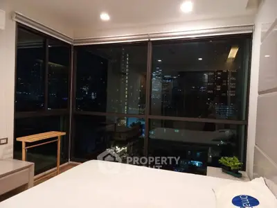Luxurious bedroom with stunning city view through large windows at night.
