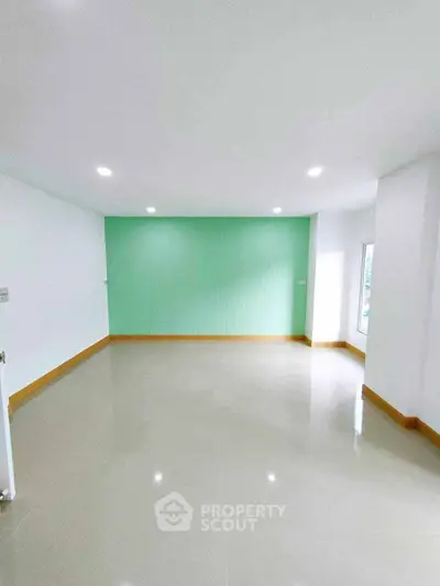 Spacious empty room with glossy tiled floor and mint green accent wall.