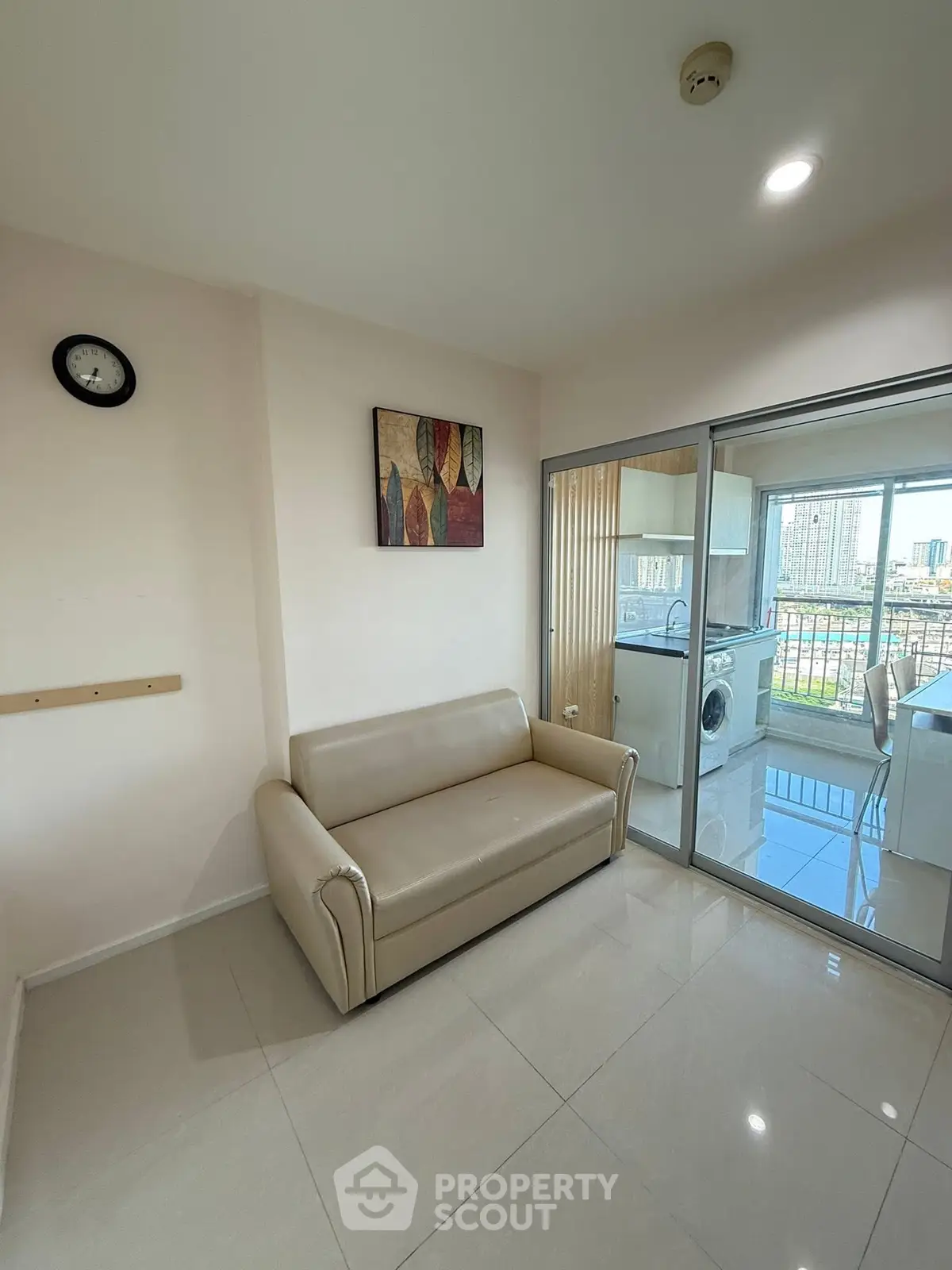 Modern living room with beige sofa and glass door leading to balcony with city view.