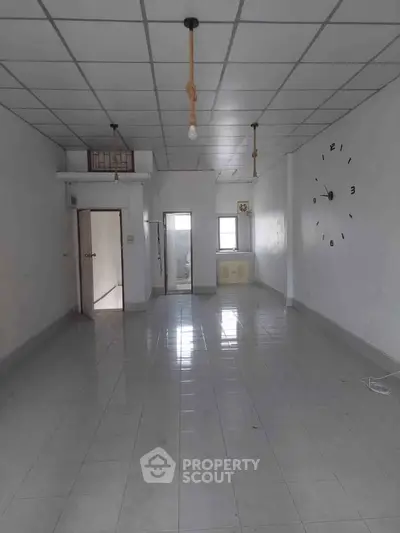 Spacious empty room with tiled flooring and wall clock, ideal for customization.
