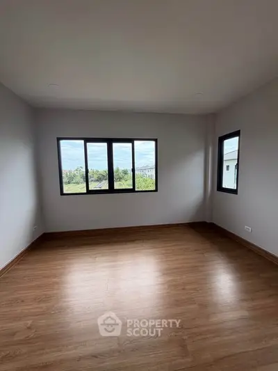 Spacious empty room with large windows and wooden flooring, offering a bright and airy atmosphere.
