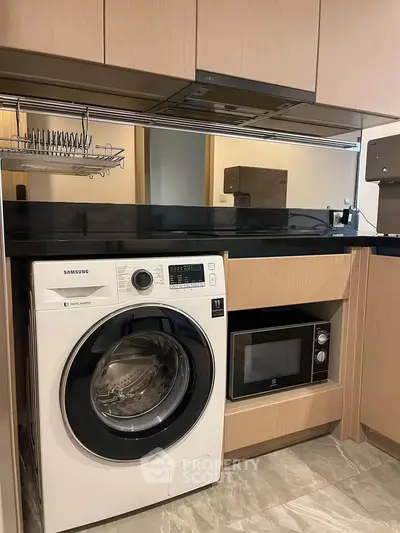 Modern kitchen with built-in appliances including washing machine and microwave, sleek cabinetry, and black countertop.