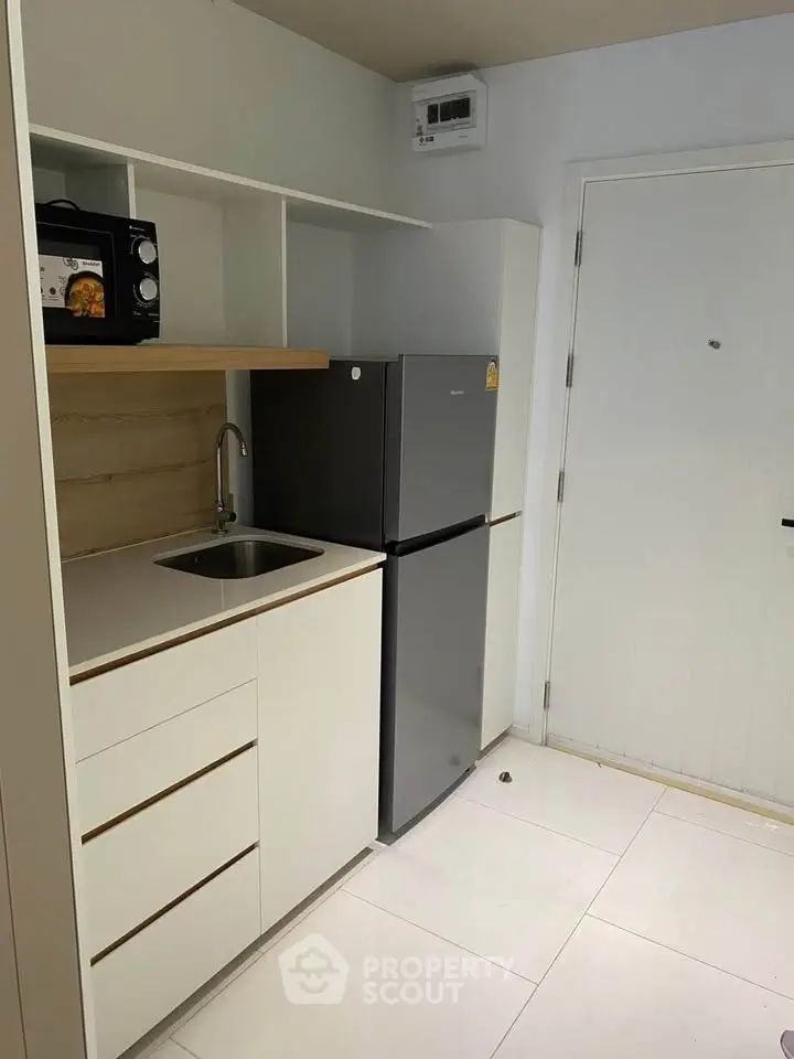 Modern compact kitchen with sleek white cabinets and stainless steel appliances in a stylish apartment.