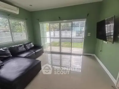 Spacious living room with sleek black sofa and wall-mounted TV, featuring large windows for natural light.