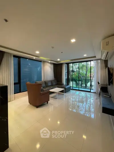 Spacious living room with large windows and modern furnishings, offering a serene view of greenery.