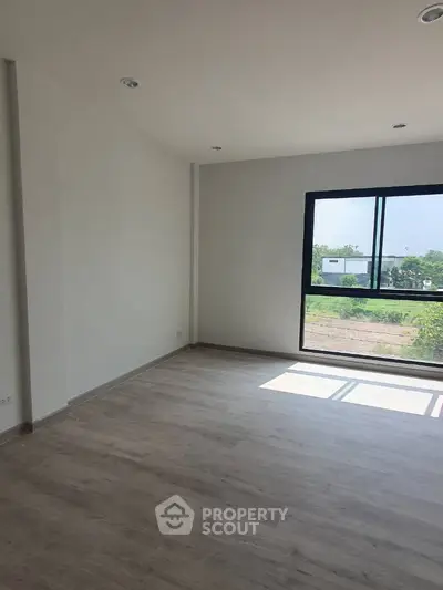 Spacious empty room with large window and wooden flooring