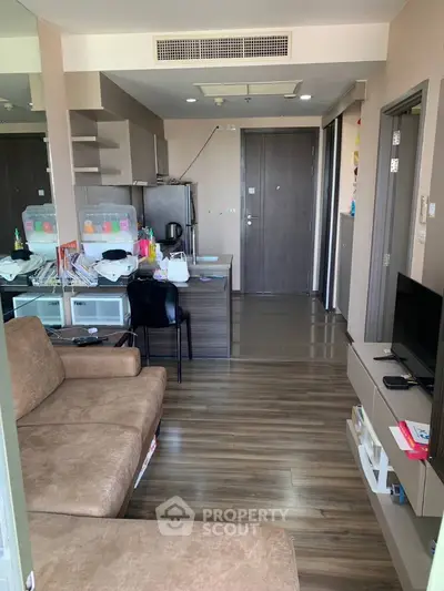 Spacious living area with sleek wooden flooring, modern furnishings, and an open layout leading to a well-equipped kitchen, perfect for urban living.