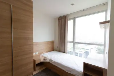 Cozy bedroom with large window and wooden furniture, offering a bright and inviting atmosphere.