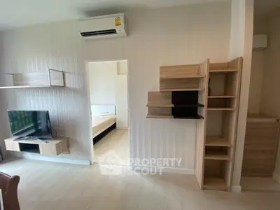 Modern living room with stylish wooden shelves and mounted TV, leading to a cozy bedroom.