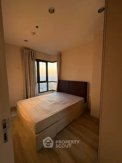 Cozy bedroom with large window offering stunning city views, featuring a comfortable bed and elegant wooden flooring.