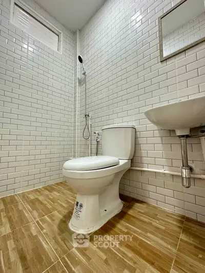 Modern bathroom with white subway tiles and wooden floor tiles, featuring a toilet, sink, and shower area.