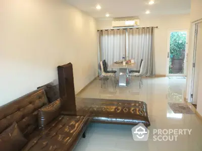 Spacious living room with glossy tiled flooring, large brown sofa, and an elegant dining area leading to a cozy garden view.