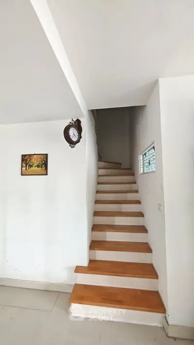 Elegant staircase with wooden steps in a modern home interior, featuring a wall clock and artwork.