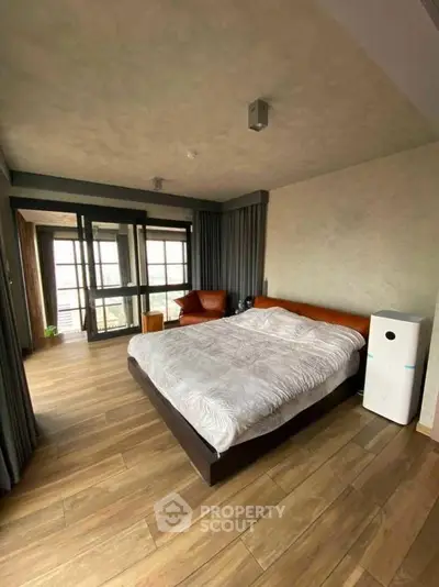 Spacious modern bedroom with wooden flooring and large windows for natural light.