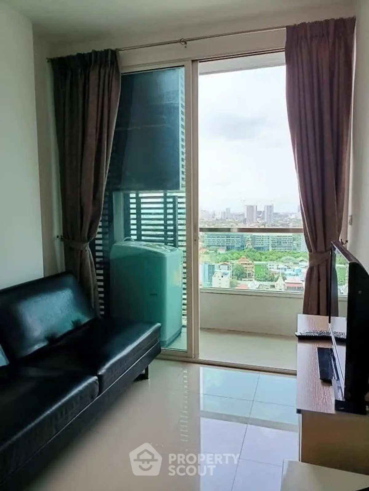 Modern living room with balcony and city view, featuring sleek black sofa and TV setup.