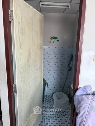 Compact bathroom with tiled walls and floor, featuring a basic toilet setup.