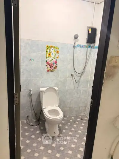 Simple bathroom with shower and toilet, featuring floral wall decoration and tiled flooring.