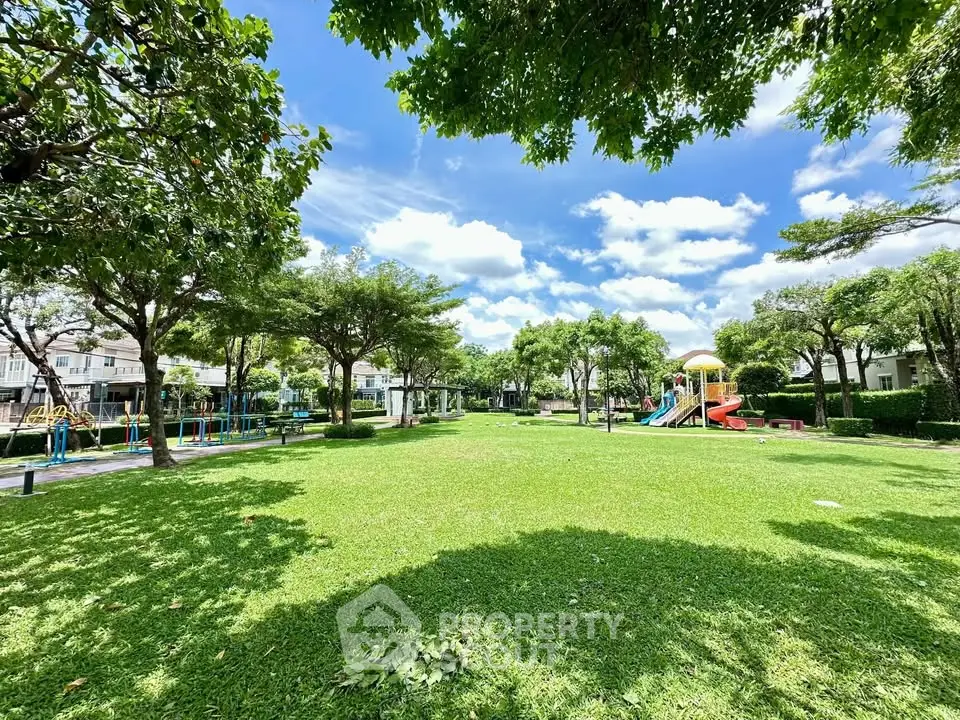 Spacious green park with playground in residential community under clear blue sky.