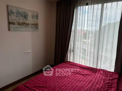 Cozy bedroom with large window and red bedding, offering natural light and serene ambiance.