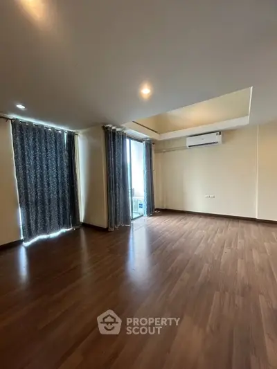 Spacious living room with wooden flooring and large windows for natural light.