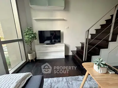 Modern living room with stylish staircase and large window, featuring a sleek TV setup and cozy decor.