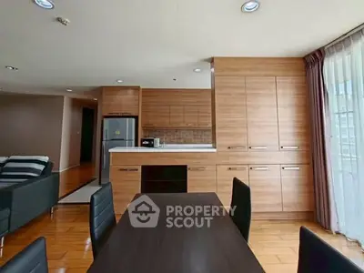 Spacious modern kitchen with wooden cabinetry and sleek dining area in open layout apartment.