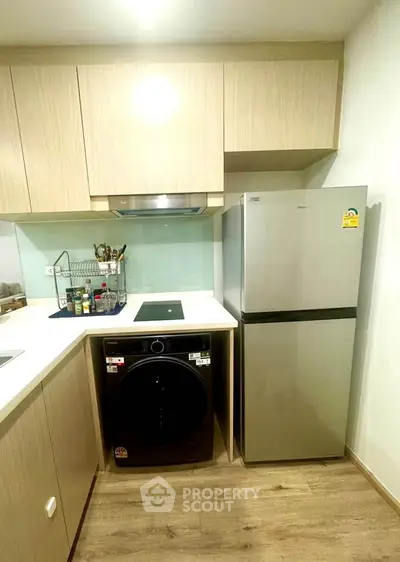 Modern kitchen with sleek appliances and wooden cabinetry, featuring a washing machine and fridge.