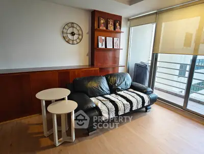 Stylish living room with black leather sofa and modern decor, featuring a balcony view.