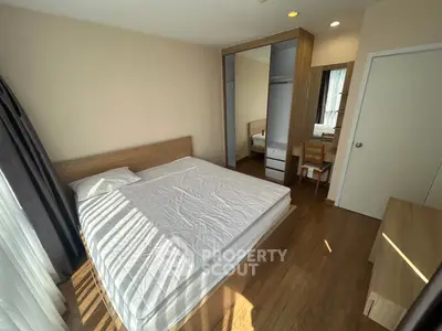 Spacious bedroom with wooden flooring and ample natural light, featuring a large bed and mirrored wardrobe.