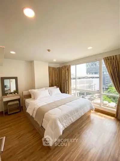 Spacious bedroom with large windows offering a stunning city view, featuring elegant wooden flooring and modern decor.