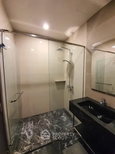 Luxurious modern bathroom with sleek black sink and elegant glass shower enclosure.