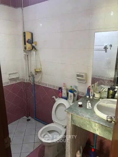 Compact bathroom with shower, toilet, and sink, featuring pink and white tiles.