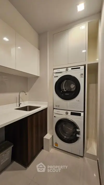 Modern laundry room with stacked washer and dryer, sleek cabinetry, and sink.