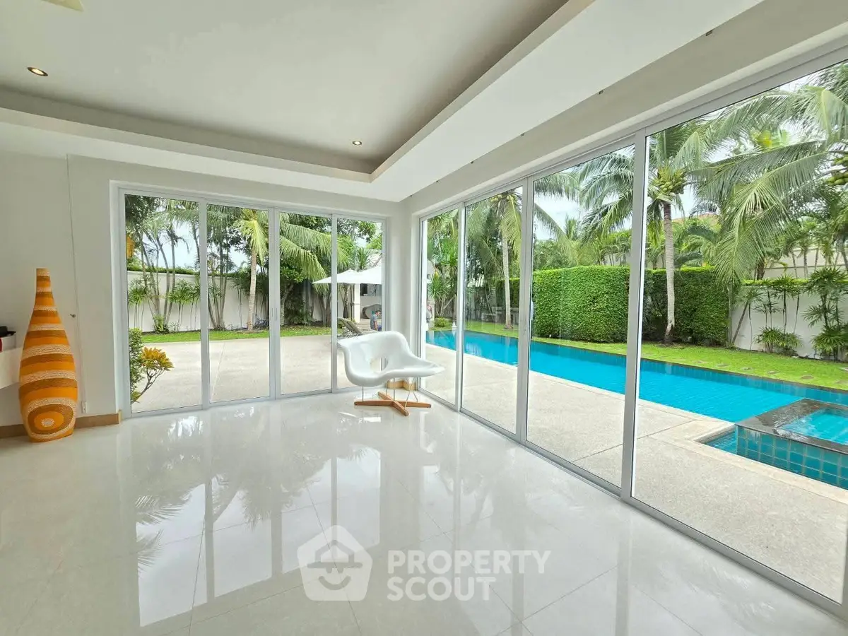 Luxurious poolside view from modern living space with floor-to-ceiling windows.