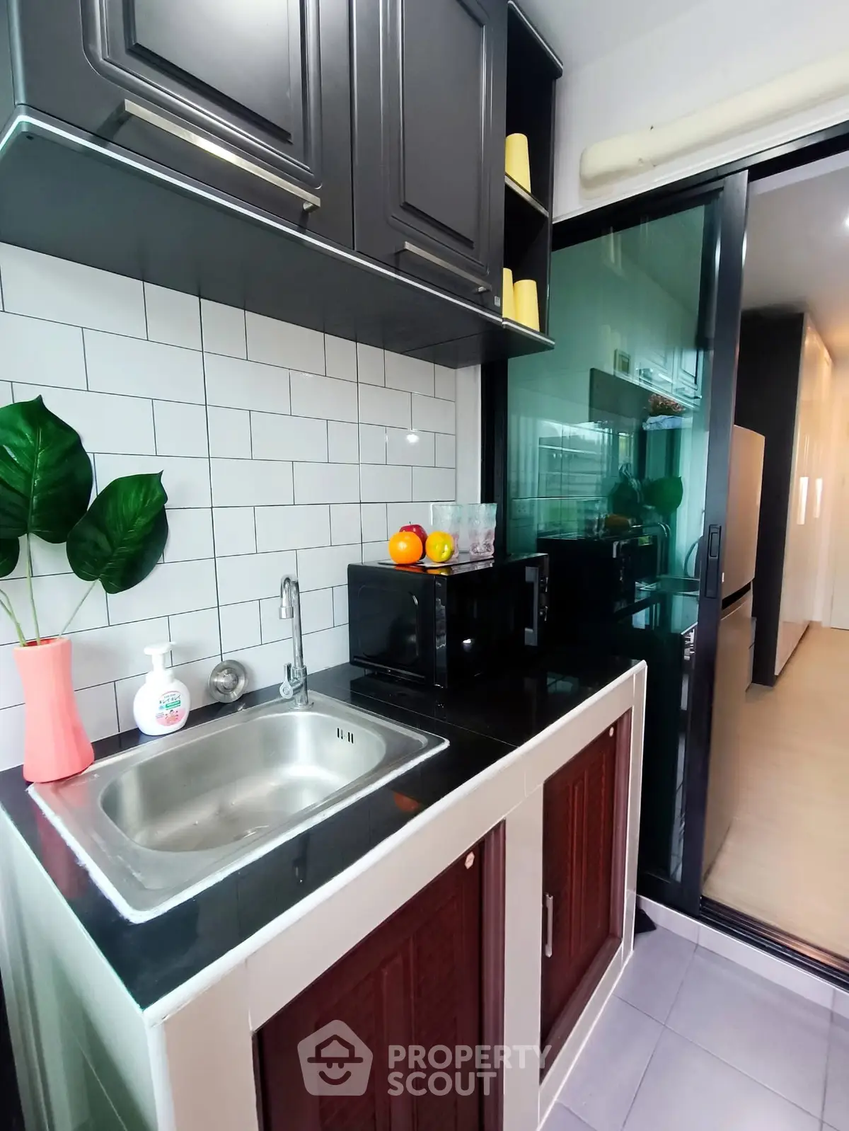 Modern kitchen with sleek black cabinets and white subway tiles, featuring a compact layout and stainless steel sink.