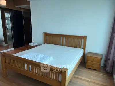 Spacious bedroom with wooden bed frame and side table, featuring large windows for natural light.