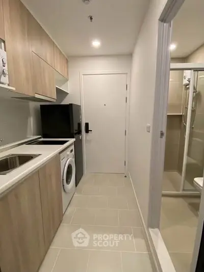 Modern compact kitchen with washing machine and fridge, adjacent to a sleek bathroom.