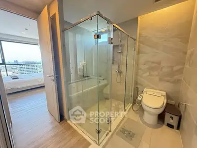 Modern bathroom with glass shower and city view from adjacent bedroom.