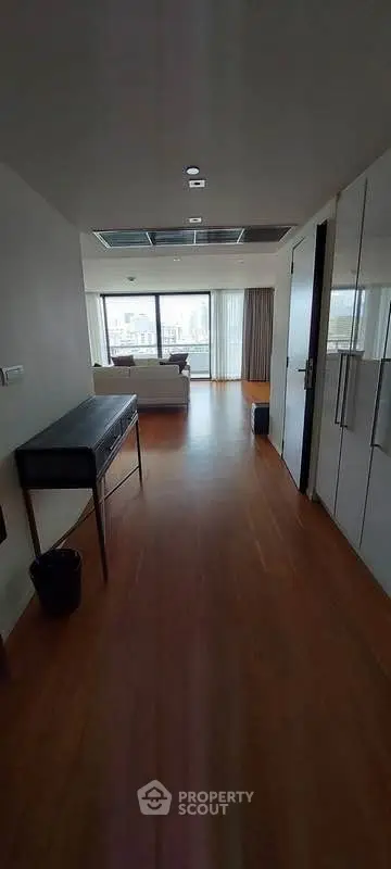 Spacious apartment hallway leading to a bright living room with large windows and balcony access.